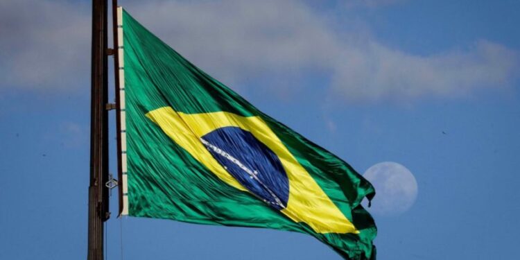 Bandeira do Brasil hasteada no mastro da Praça dos Três Poderes, tendo a lua ao fundo