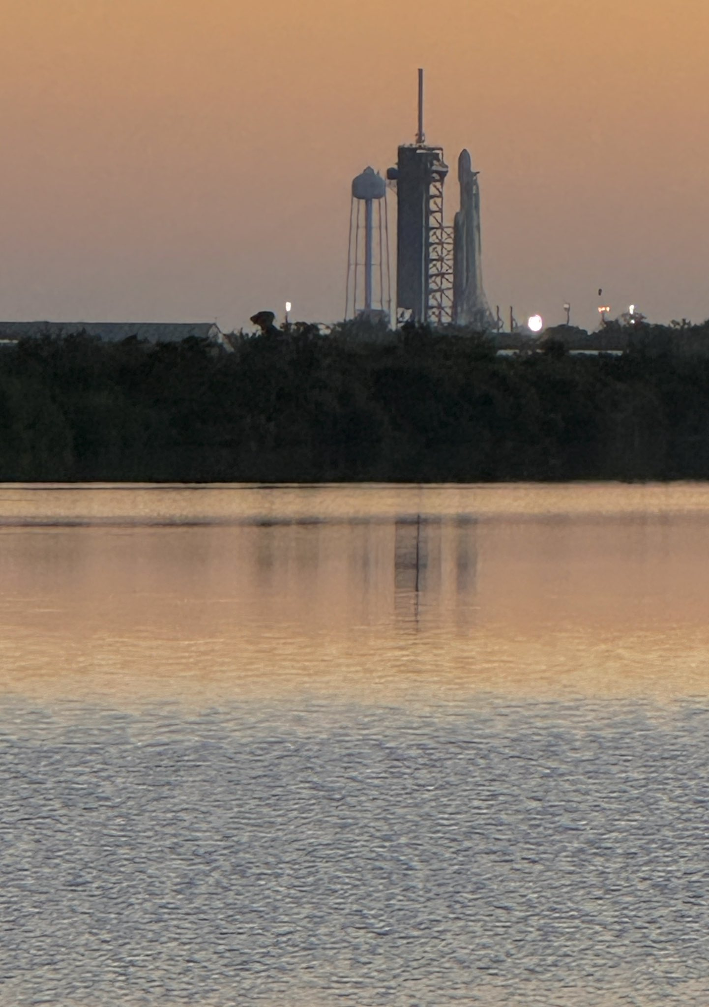 A SpaceX Falcon Heavy rocket on the launch pad at dawn with its reflection in the bay nearby