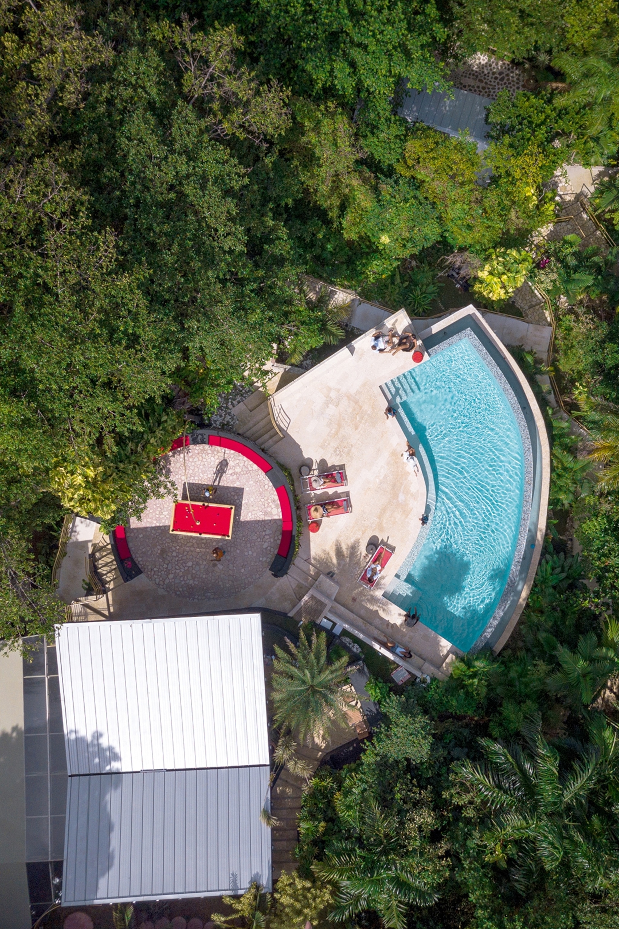 Aerial view of a pool and people on sunloungers in the middle of the jungle