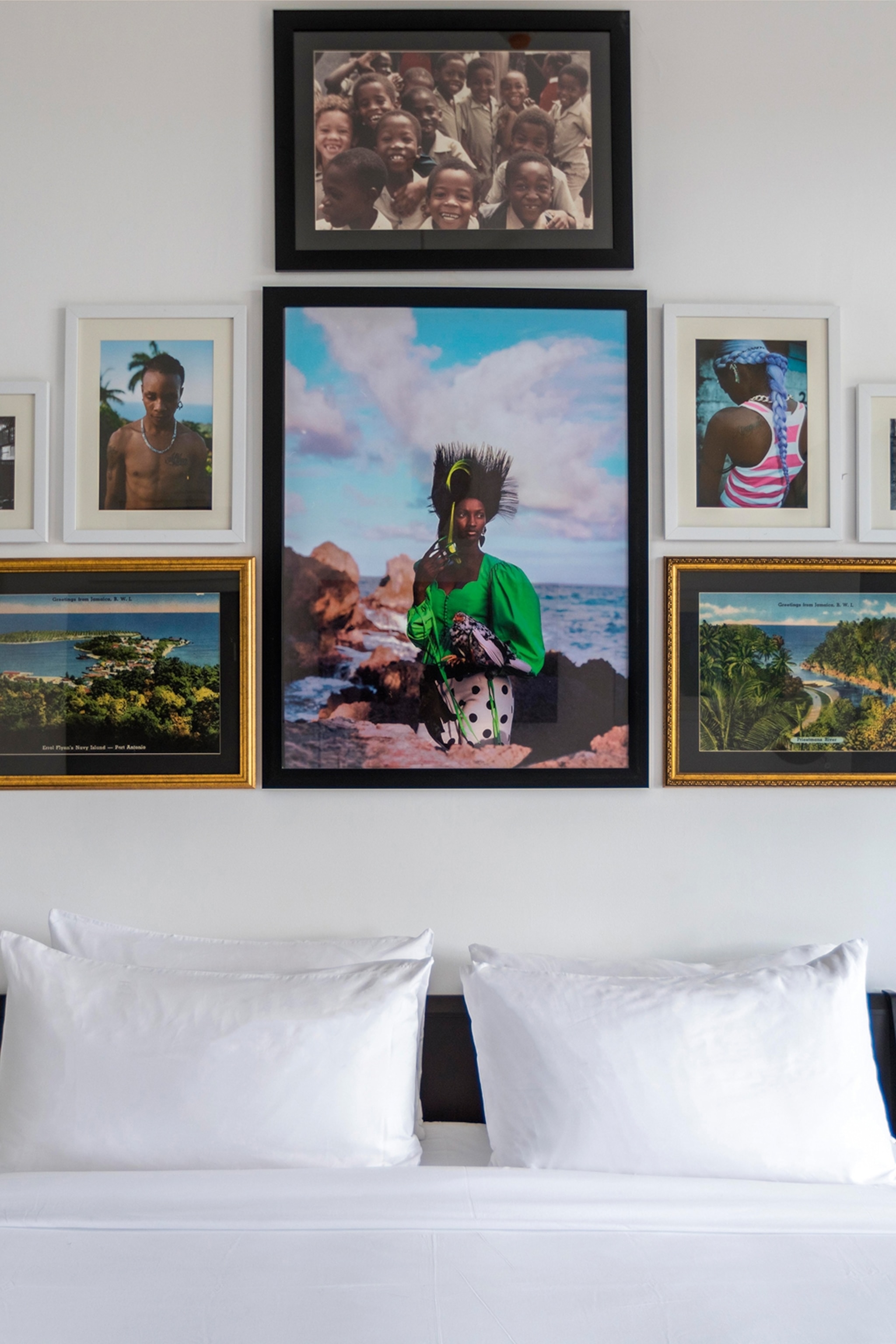 White bedspread with a black headboard and paintings and photographs hung in frames above